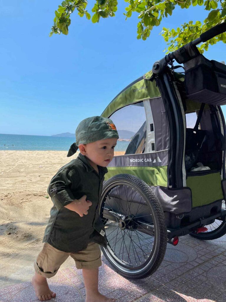 Green Nordic Cab Explorer kids bike trailer for kids on the beach in Vietnam. 