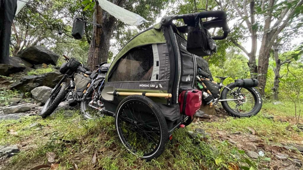 Bicycle trailer for kids modified and rigged for long trips. Green Nordic Cab Explorer in the woods in Vietnam. Bikepacking
